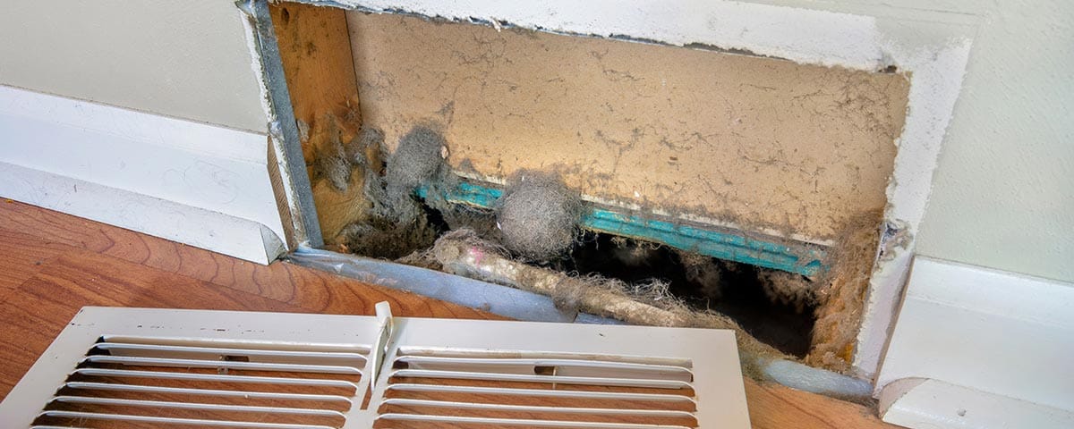 Close-up of a dirty furnace vent and air duct filled with dust and debris.