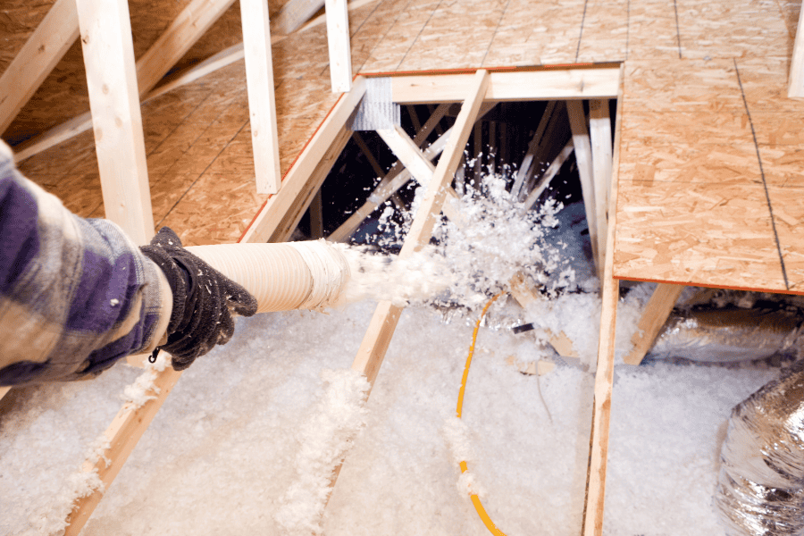 Technician applying blown-in insulation across attic floor