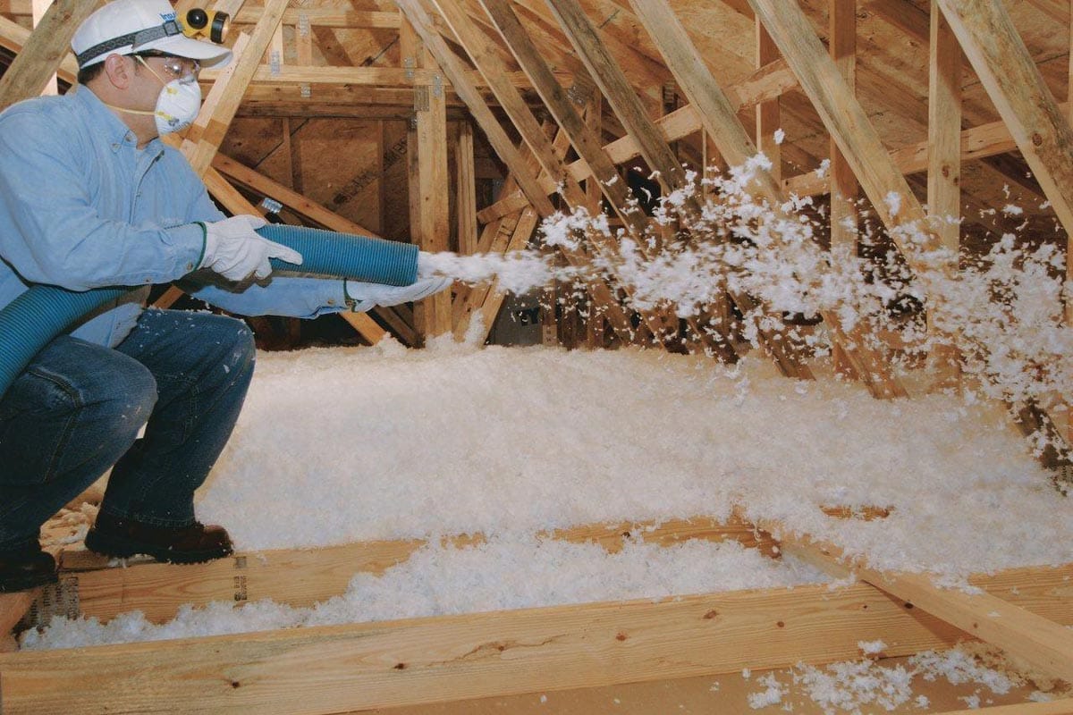 Blown-in fiberglass insulation being applied in attic space