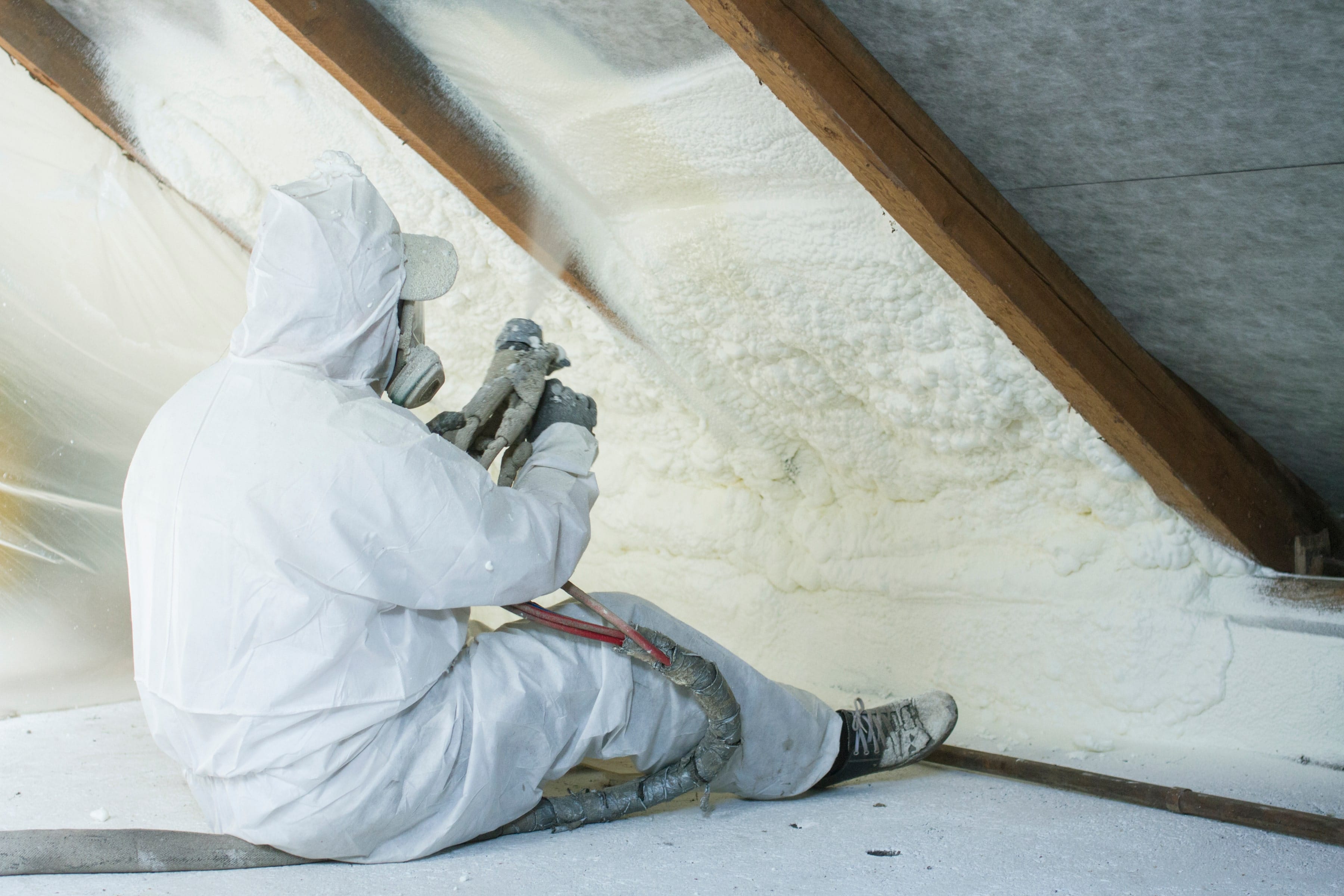 Worker applying spray foam insulation in attic