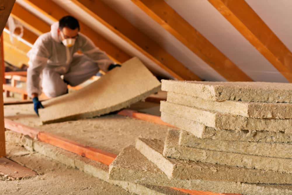 Alt text: Professional removing old attic insulation with protective gear and vacuum system.