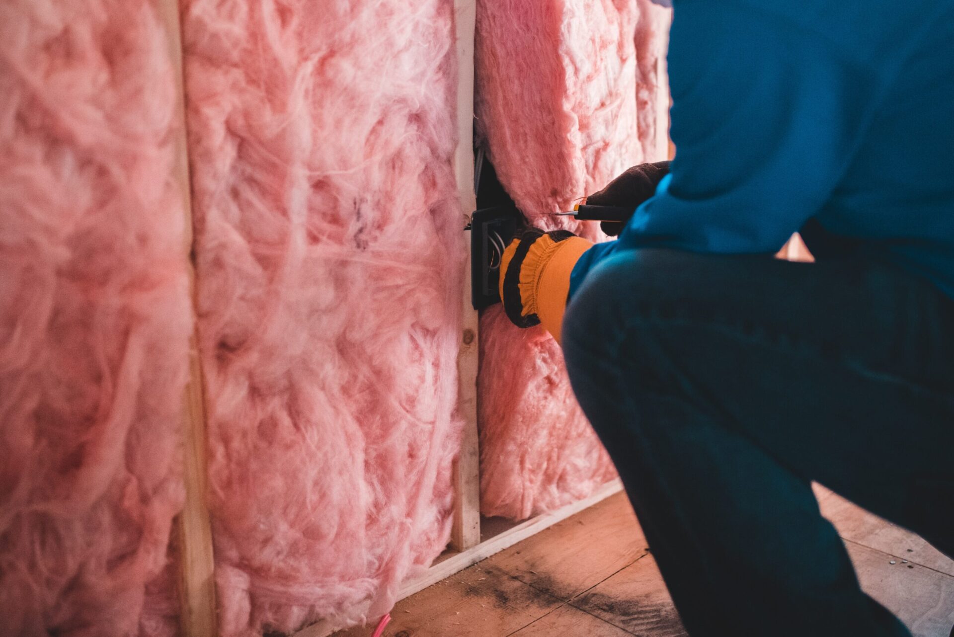 Worker installing fiberglass insulation inside wall cavity
