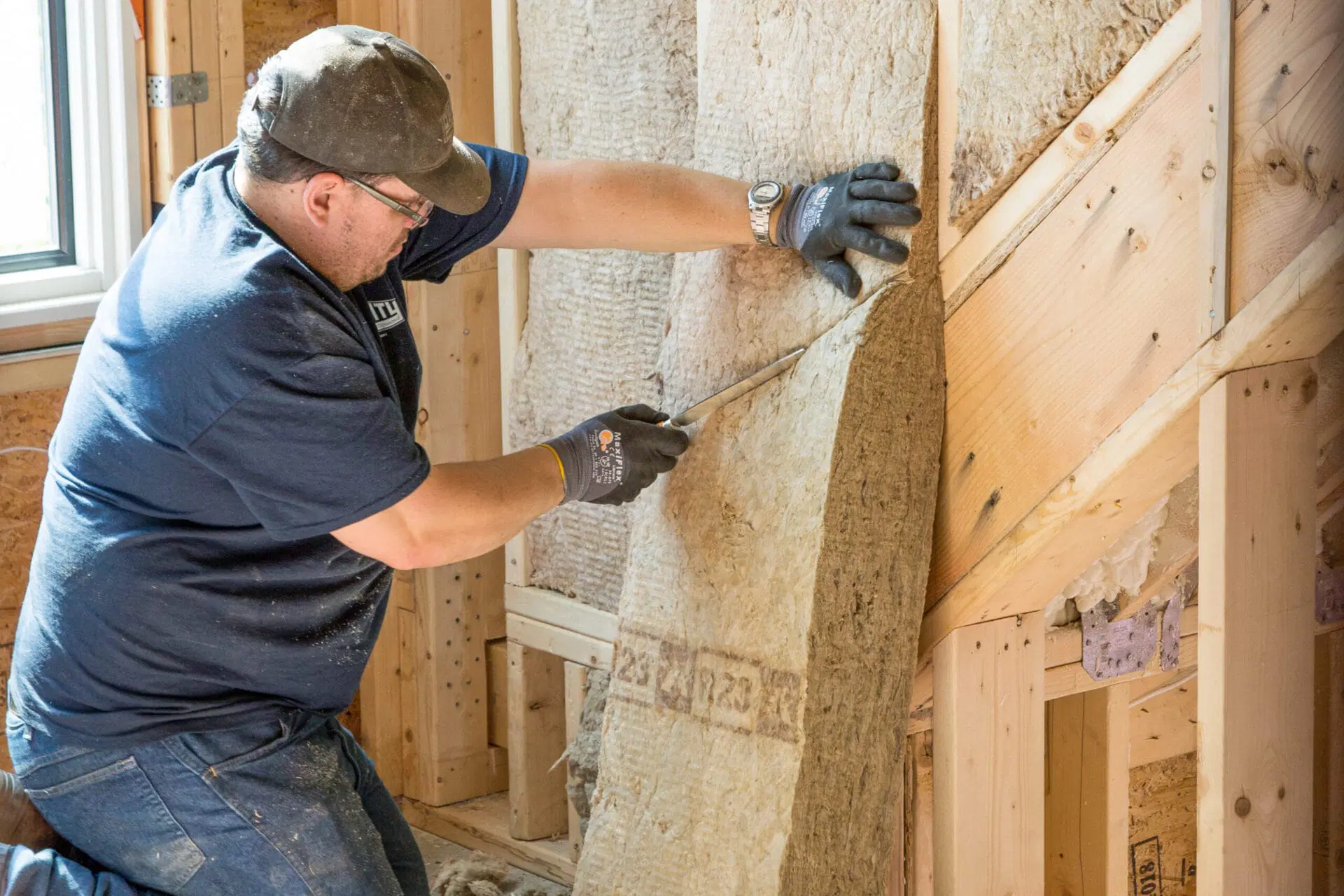 Contractor installing batt insulation inside unfinished residential wall framing. 