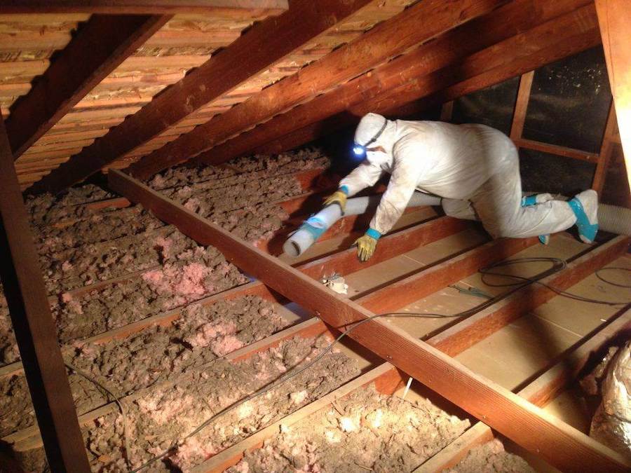 Attic insulation being removed with a vacuum hose.