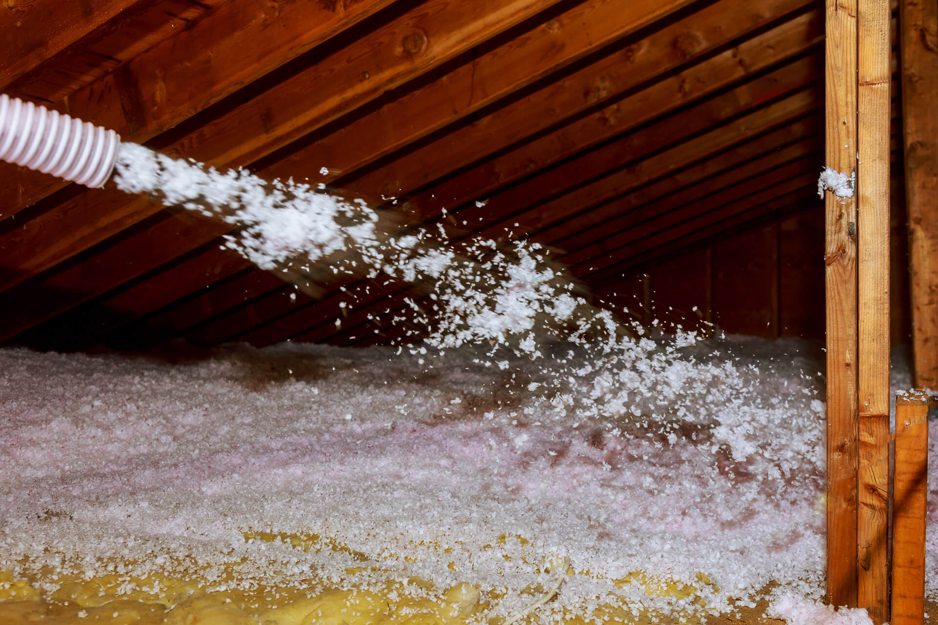 Close-up action shot of loose-fill insulation being blown across wooden attic joists