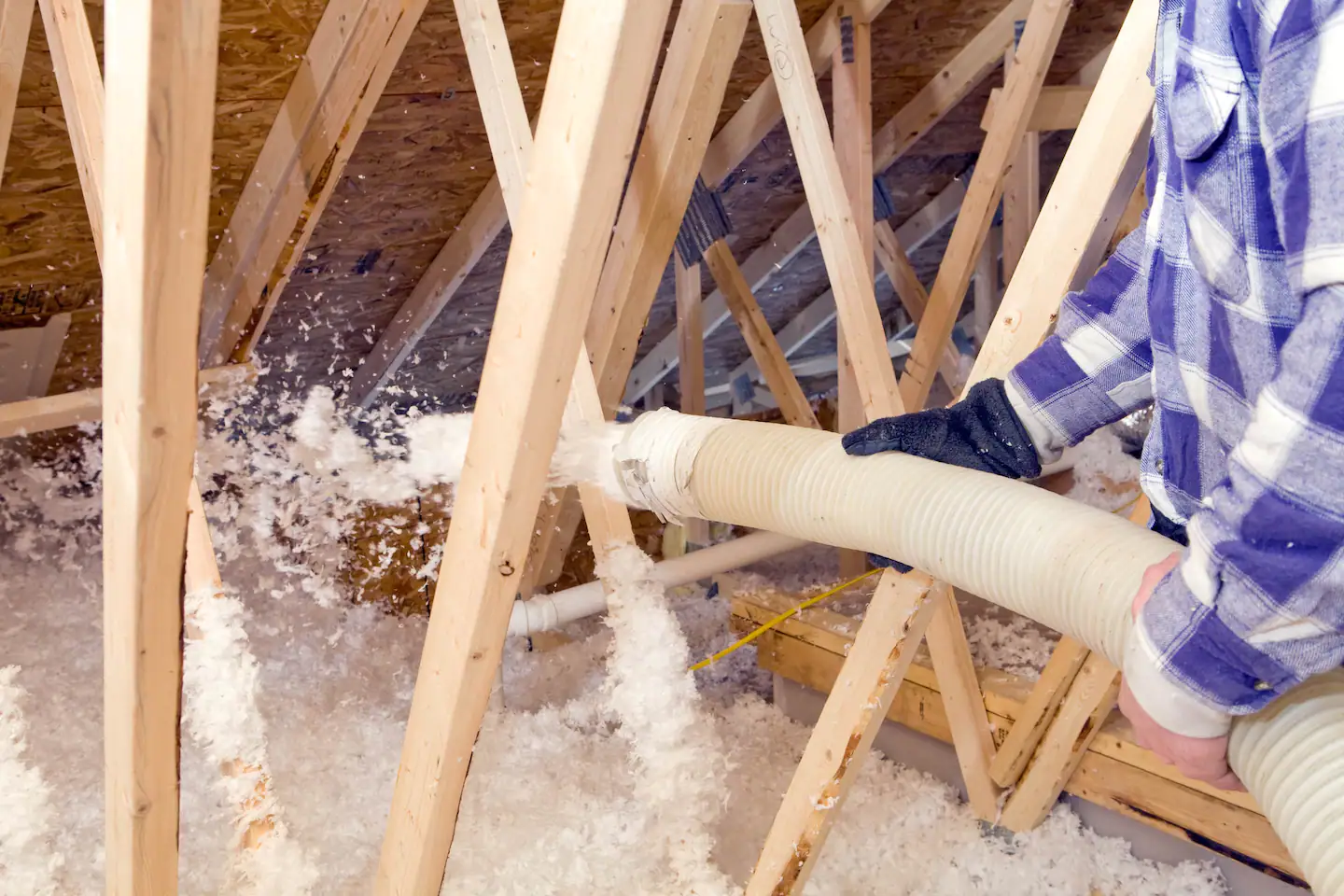 Close-up of loose-fill blown-in fiberglass insulation spraying across an attic floor frame