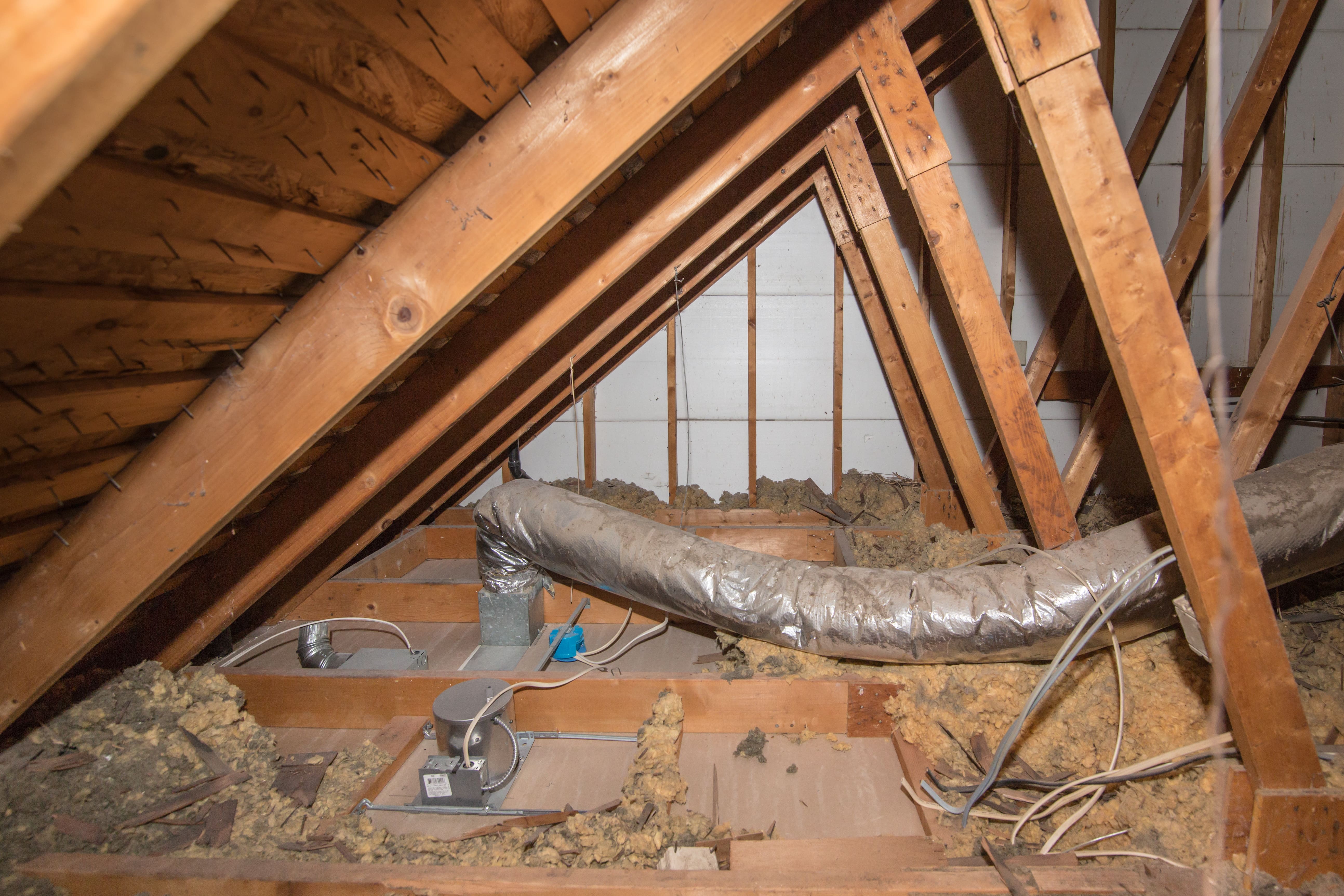 Close-up of wooden roof rafters, silver air duct, and electrical housings inside an unfinished residential attic